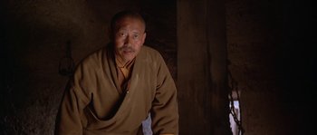 Movie still from “Kundun” (1997), directed by Martin Scorsese – An older man wearing a brown robe in a dark room; Close Up shot, Low angle