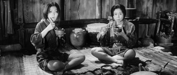 Movie still from “Black Cat” (1968), directed by Kaneto Shindô – Two women sitting on the ground eating food; Medium shot, Low angle
