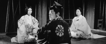 Movie still from “Black Cat” (1968), directed by Kaneto Shindô – A man in a kimono sitting in front of two women; Medium shot, Low angle