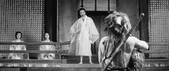 Movie still from “Black Cat” (1968), directed by Kaneto Shindô – A man dressed in a white robe holding a sword in front of two other men; Medium shot, Over the shoulder angle