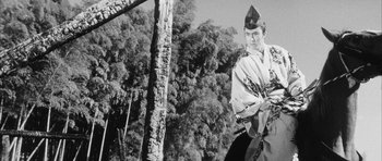 Movie still from “Black Cat” (1968), directed by Kaneto Shindô – A man in a toga stands in front of a tree; Medium shot, Low angle