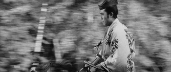 Movie still from “Black Cat” (1968), directed by Kaneto Shindô – A man riding a motorcycle down a street; Medium shot, Low angle