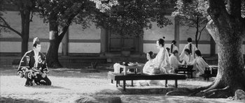Movie still from “Black Cat” (1968), directed by Kaneto Shindô – Two women sitting on top of a wooden bench in front of a tree; Wide shot, High angle