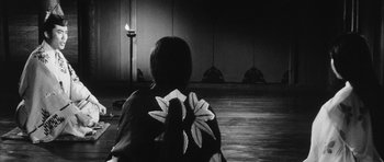 Movie still from “Black Cat” (1968), directed by Kaneto Shindô – A person in a black and white photo with a candle in the background; Wide shot, Over the shoulder angle