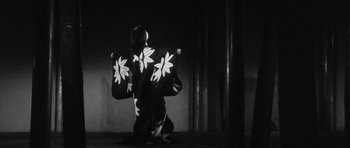 Movie still from “Black Cat” (1968), directed by Kaneto Shindô – A person holding a flag in a dark room; Wide shot, Low angle