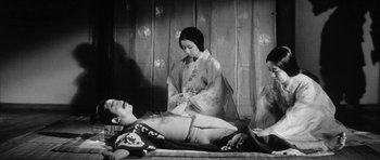 Movie still from “Black Cat” (1968), directed by Kaneto Shindô – An old photo of a man laying on a bed next to two women; Medium shot, Low angle