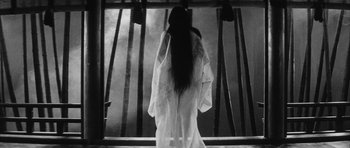 Movie still from “Black Cat” (1968), directed by Kaneto Shindô – A woman standing in front of a window with her hair hanging down; Medium shot, Low angle