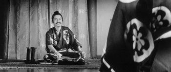 Movie still from “Black Cat” (1968), directed by Kaneto Shindô – A man sitting on the ground wearing a kimono; Medium shot, High angle