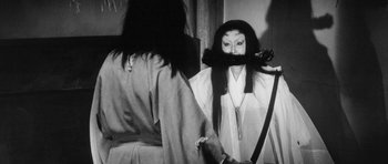 Movie still from “Black Cat” (1968), directed by Kaneto Shindô – A person with long black hair holding a sword in front of a mirror; Medium shot, Over the shoulder angle