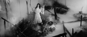 Movie still from “Black Cat” (1968), directed by Kaneto Shindô – A woman in a robe holding a sword in front of a fire pit; Wide shot, High angle