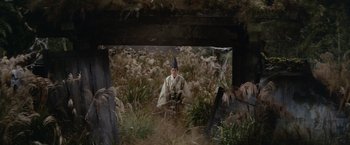 Movie still from “Kwaidan” (1964), directed by Masaki Kobayashi – A man wearing a hat sitting in the grass; Wide shot, High angle