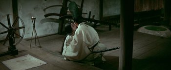 Movie still from “Kwaidan” (1964), directed by Masaki Kobayashi – A person sitting on the ground holding a sword; Wide shot, High angle