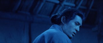 Movie still from “Kwaidan” (1964), directed by Masaki Kobayashi – A man in a blue shirt is standing in a dark room; Close Up shot, Low angle