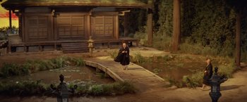 Movie still from “Kwaidan” (1964), directed by Masaki Kobayashi – A man sitting on top of a wooden bridge in front of a house; Extreme Wide shot, High angle