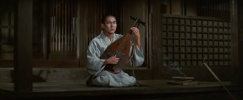 Movie still from “Kwaidan” (1964), directed by Masaki Kobayashi – A man sitting on the ground holding a musical instrument; Medium shot, Low angle