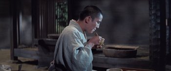 Movie still from “Kwaidan” (1964), directed by Masaki Kobayashi – A man holding a bowl of food while sitting in a chair; Medium shot, High angle
