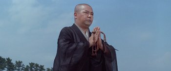 Movie still from “Kwaidan” (1964), directed by Masaki Kobayashi – A bald man in a black robe holding his hands in prayer; Medium shot, Low angle