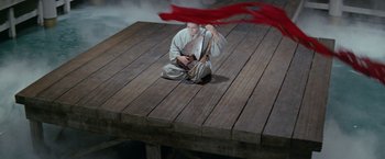 Movie still from “Kwaidan” (1964), directed by Masaki Kobayashi – A person sitting on a dock with a red cloth; Extreme Wide shot, High angle