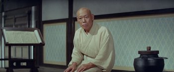 Movie still from “Kwaidan” (1964), directed by Masaki Kobayashi – An older man in a white robe sitting on a chair; Medium shot, Low angle