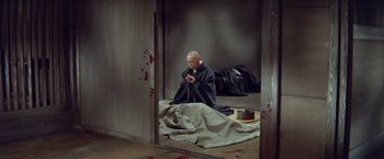 Movie still from “Kwaidan” (1964), directed by Masaki Kobayashi – A man sitting on the ground looking at his cell phone; Wide shot, High angle
