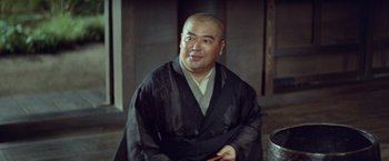 Movie still from “Kwaidan” (1964), directed by Masaki Kobayashi – A man in a black robe sitting in front of a wall; Medium shot, Low angle