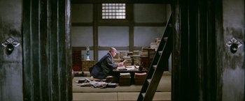 Movie still from “Kwaidan” (1964), directed by Masaki Kobayashi – A man sitting at a table in front of stacks of books; Wide shot, High angle