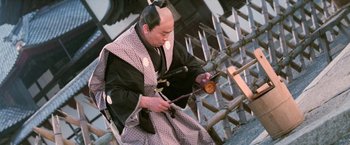 Movie still from “Kwaidan” (1964), directed by Masaki Kobayashi – An older man in traditional japanese garb using an instrument; Medium shot, High angle