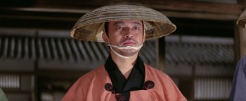 Movie still from “Kwaidan” (1964), directed by Masaki Kobayashi – A man wearing a straw hat and a black and orange outfit; Close Up shot, Low angle