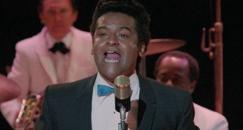A man in a suit and bow tie singing into a microphone