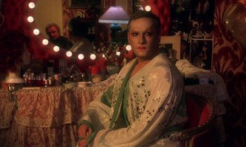 Movie still from “La Cage aux Folles” (1978), directed by Édouard Molinaro – A woman sitting in front of a table with lights in the background; Medium shot, Over the shoulder angle