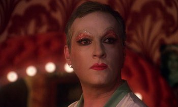 Movie still from “La Cage aux Folles” (1978), directed by Édouard Molinaro – A man with a very bright make - up is looking into the camera; Close Up shot, Over the shoulder angle
