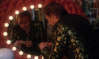 Movie still from “La Cage aux Folles” (1978), directed by Édouard Molinaro – A man looking at his cell phone in front of a mirror; Medium shot, Over the shoulder angle