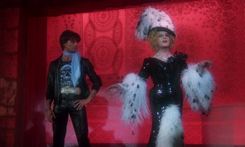 Movie still from “La Cage aux Folles” (1978), directed by Édouard Molinaro – A man standing next to a woman in a black dress; Wide shot, Over the shoulder angle
