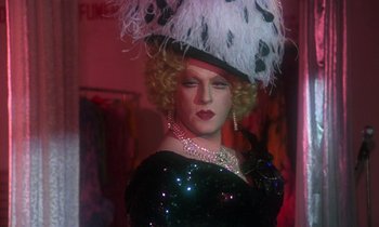 Movie still from “La Cage aux Folles” (1978), directed by Édouard Molinaro – A woman in a black dress and a white hat; Close Up shot, Over the shoulder angle