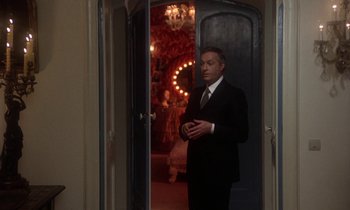 Movie still from “La Cage aux Folles” (1978), directed by Édouard Molinaro – A man in a black suit standing in front of an open door; Medium shot, Over the shoulder angle