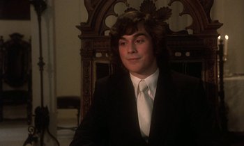 Movie still from “La Cage aux Folles” (1978), directed by Édouard Molinaro – A man in a suit and tie sitting in front of an ornate chair; Close Up shot, Low angle