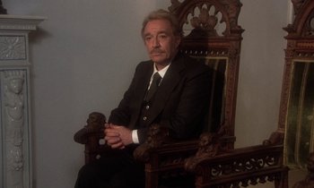 Movie still from “La Cage aux Folles” (1978), directed by Édouard Molinaro – An older man in a suit sitting in a wooden chair; Medium shot, High angle
