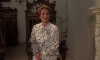 Movie still from “La Cage aux Folles” (1978), directed by Édouard Molinaro – A woman sitting in a chair wearing a polka dot blouse; Medium shot, Low angle