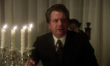 Movie still from “La Cage aux Folles” (1978), directed by Édouard Molinaro – A man wearing a suit and tie holding a candle holder; Close Up shot, Low angle