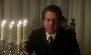 Movie still from “La Cage aux Folles” (1978), directed by Édouard Molinaro – A man wearing a suit and tie sitting in front of candles; Close Up shot, Low angle