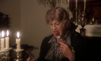 Movie still from “La Cage aux Folles” (1978), directed by Édouard Molinaro – An older woman is eating a fork with her mouth; Close Up shot, Over the shoulder angle