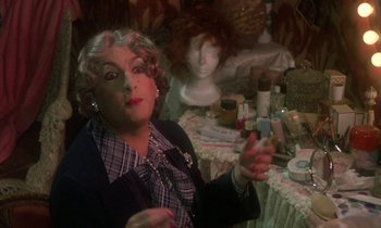 Movie still from “La Cage aux Folles” (1978), directed by Édouard Molinaro – A woman in a wig sitting in front of a table; Close Up shot, Over the shoulder angle