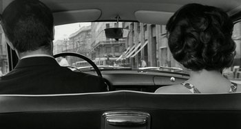 Movie still from “La Notte” (1961), directed by Michelangelo Antonioni – A man driving a car in the back of a car; Medium shot, Over the shoulder angle