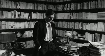 Movie still from “La Notte” (1961), directed by Michelangelo Antonioni – A man standing in front of a book shelf; Medium shot, High angle