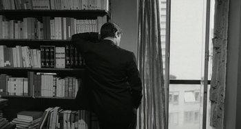 Movie still from “La Notte” (1961), directed by Michelangelo Antonioni – A black and white photo of a man in a suit looking at books; Medium shot, Over the shoulder angle