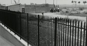 Movie still from “La Notte” (1961), directed by Michelangelo Antonioni – A black and white photo of a fence with a person in the background; Extreme Wide shot, High angle