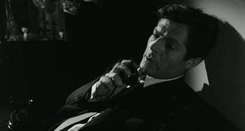 Movie still from “La Notte” (1961), directed by Michelangelo Antonioni – A black and white photo of a man smoking a cigarette; Close Up shot, High angle