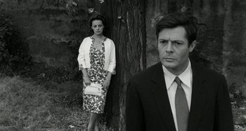 Movie still from “La Notte” (1961), directed by Michelangelo Antonioni – A man and a woman standing next to a tree; Medium shot, Low angle