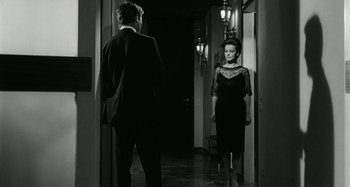 Movie still from “La Notte” (1961), directed by Michelangelo Antonioni – A man and a woman are standing in a hallway; Medium shot, Over the shoulder angle