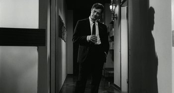 Movie still from “La Notte” (1961), directed by Michelangelo Antonioni – A black and white photo of a man in a suit looking at his cell phone; Medium shot, Low angle